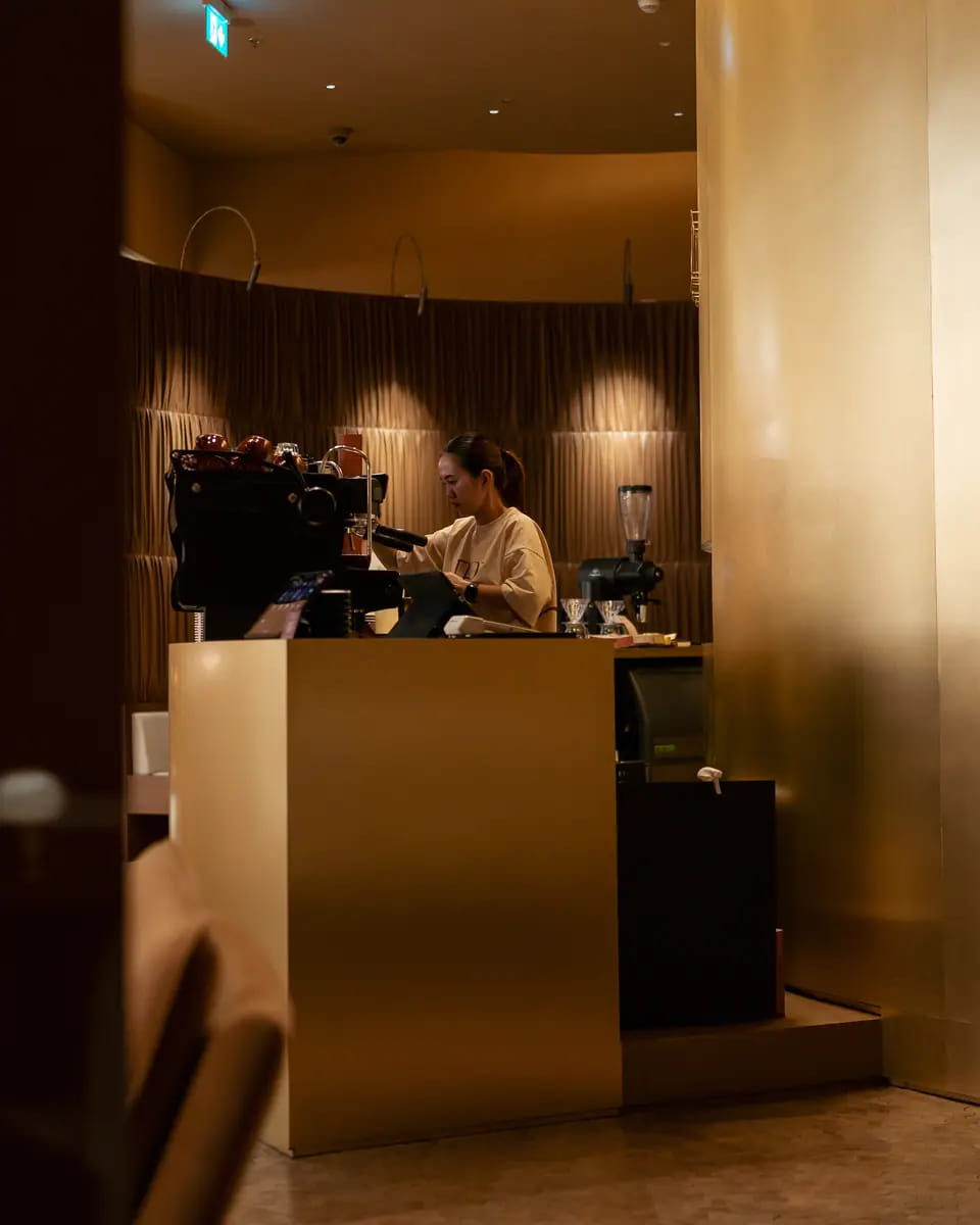 TRIO's curved brushed-gold counter at Dubai Mall under warm downlights, the espresso bar behind