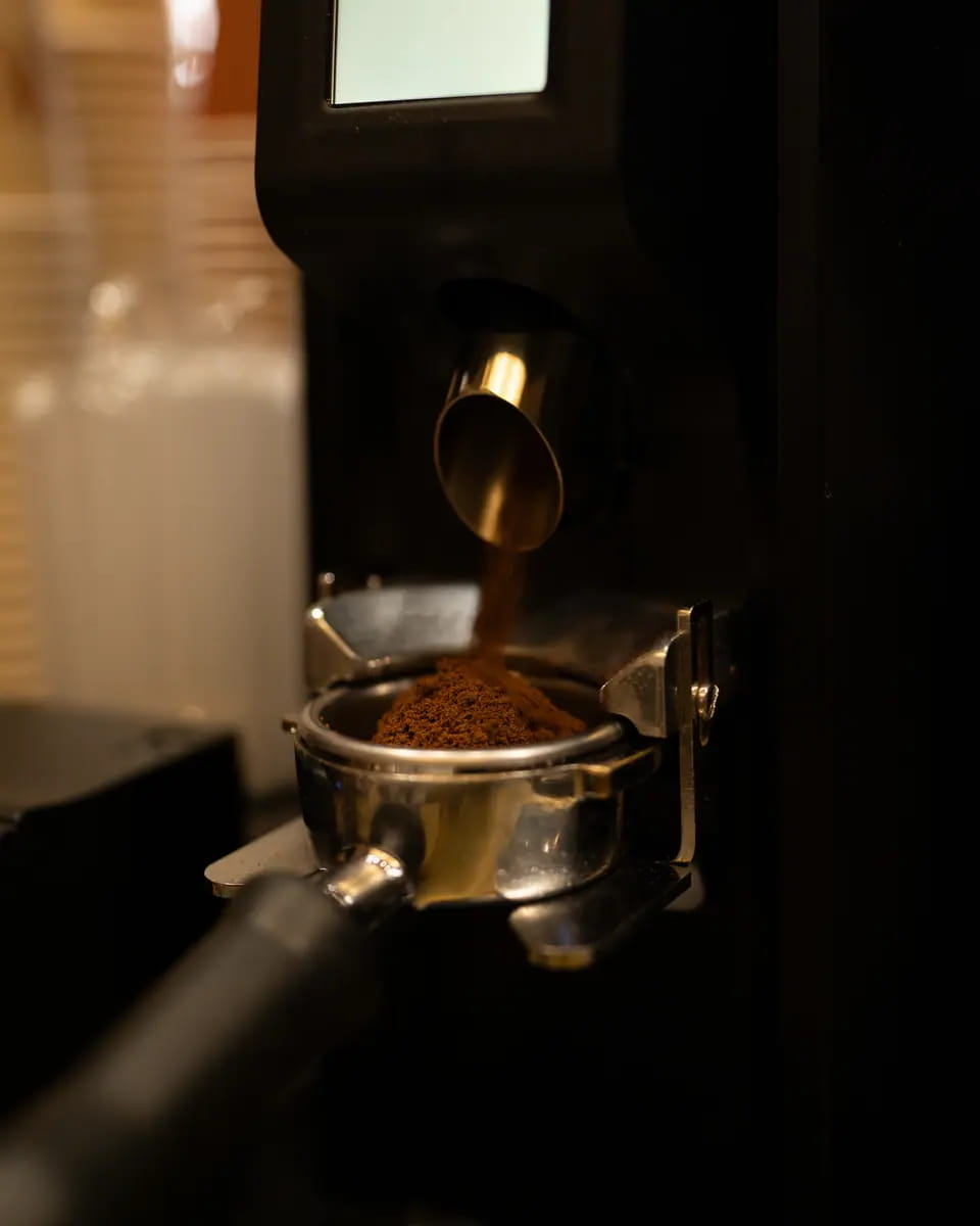 Fresh grounds falling from the grinder into a portafilter in low, warm light