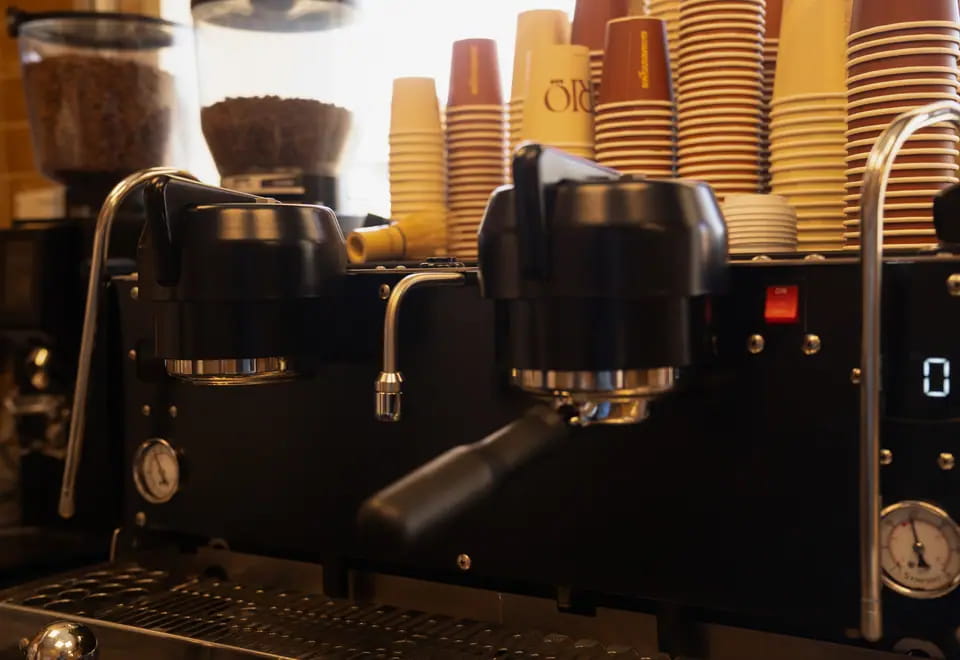 Twin espresso group heads with stacks of terracotta and gold TRIO cups on the machine behind