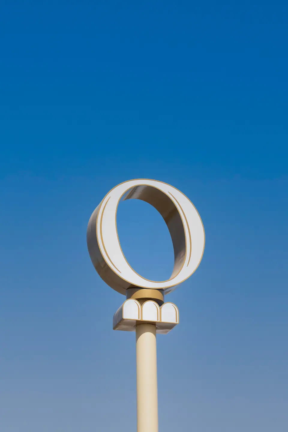 TRIO's cream O-and-three-arches pylon at TRIO Lagoon Stop, Mina Al Arab, Ras Al Khaimah, against a deep blue sky