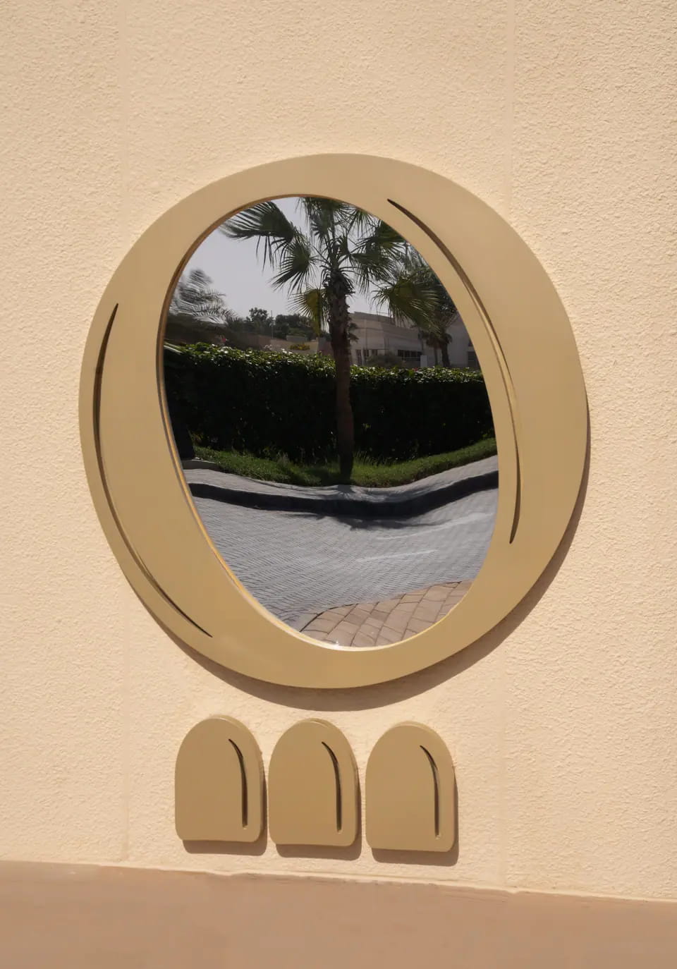 An oval brass-rimmed porthole set into the rendered wall, palms reflected in it, with three small arch forms beneath