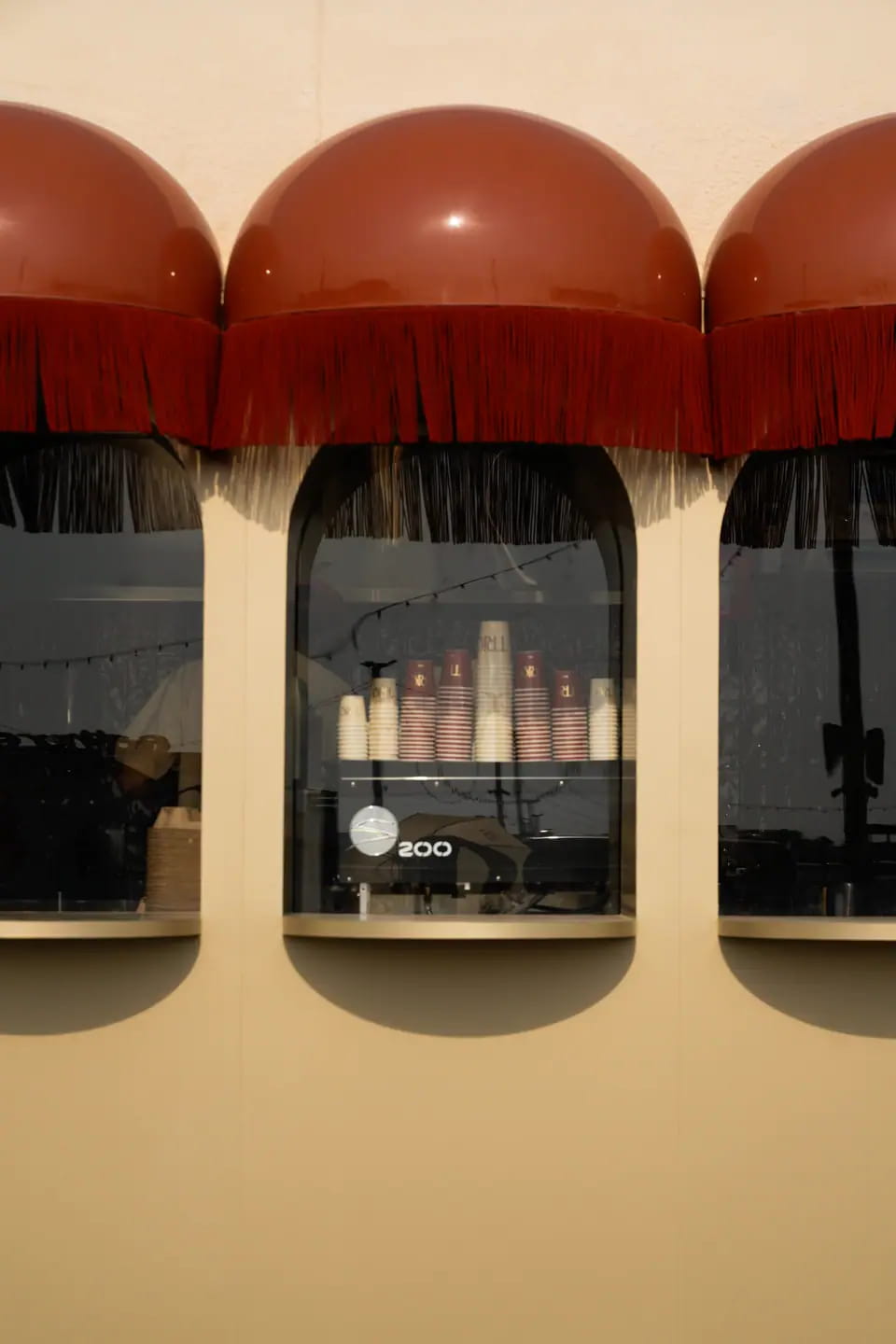 Three arched windows under glossy red dome awnings with fringe, set into a warm cream wall