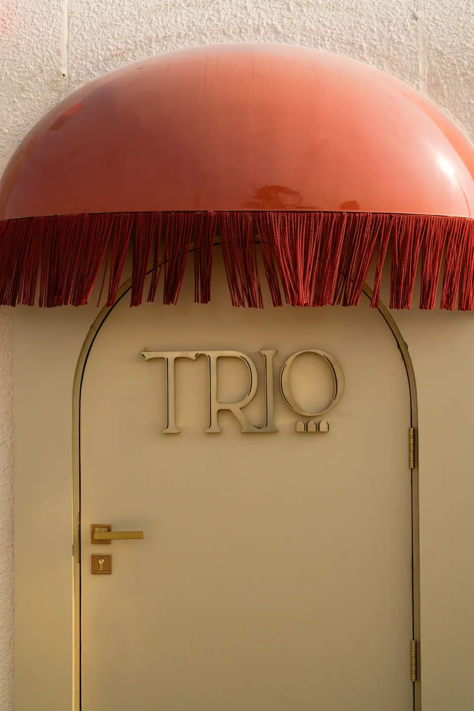 An arched cream door with a gold TRIO wordmark beneath a red domed, fringed awning