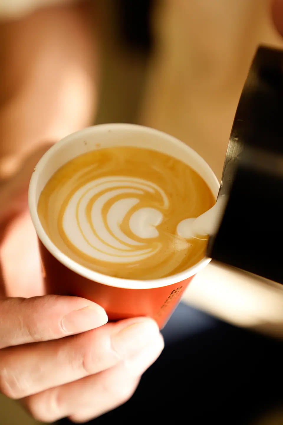 Milk poured into a terracotta TRIO cup, forming a rosetta in warm light