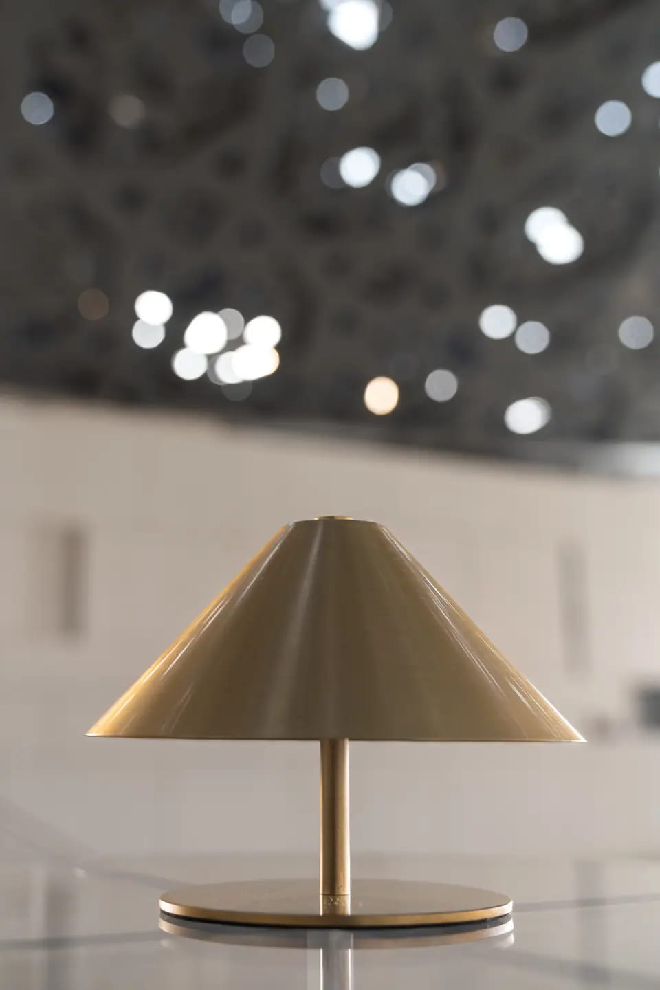A small brass cone table lamp on a white surface, points of light from the dome blurred into bokeh behind it