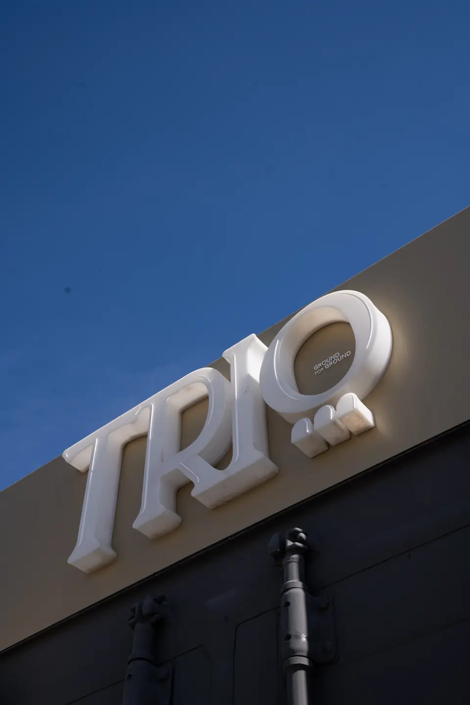 Looking up at the TRIO wordmark in white relief along the top of the container, its door locking bars below and deep blue sky above