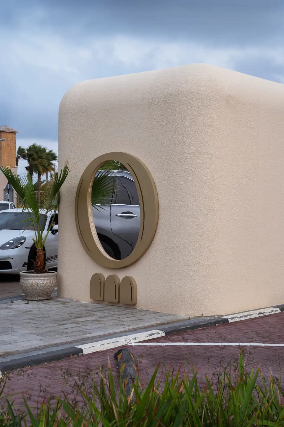 The rounded end of the cream container with an oval brass-framed porthole and three small arches beneath, a potted palm beside it
