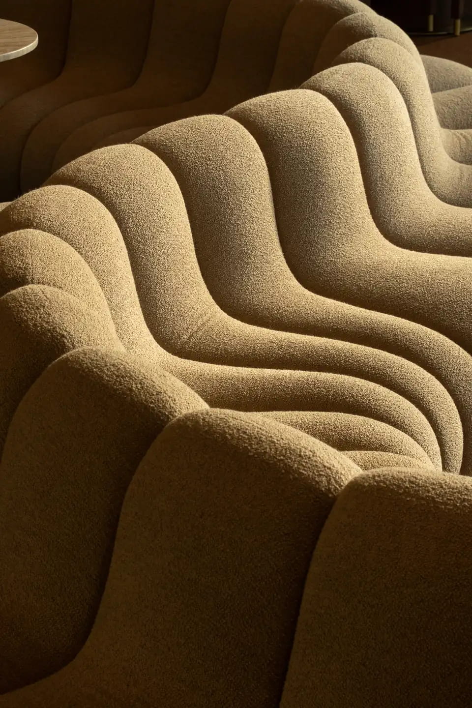 Close in on the lounge sofa: deep boucle ripples in sand and ochre, catching low light