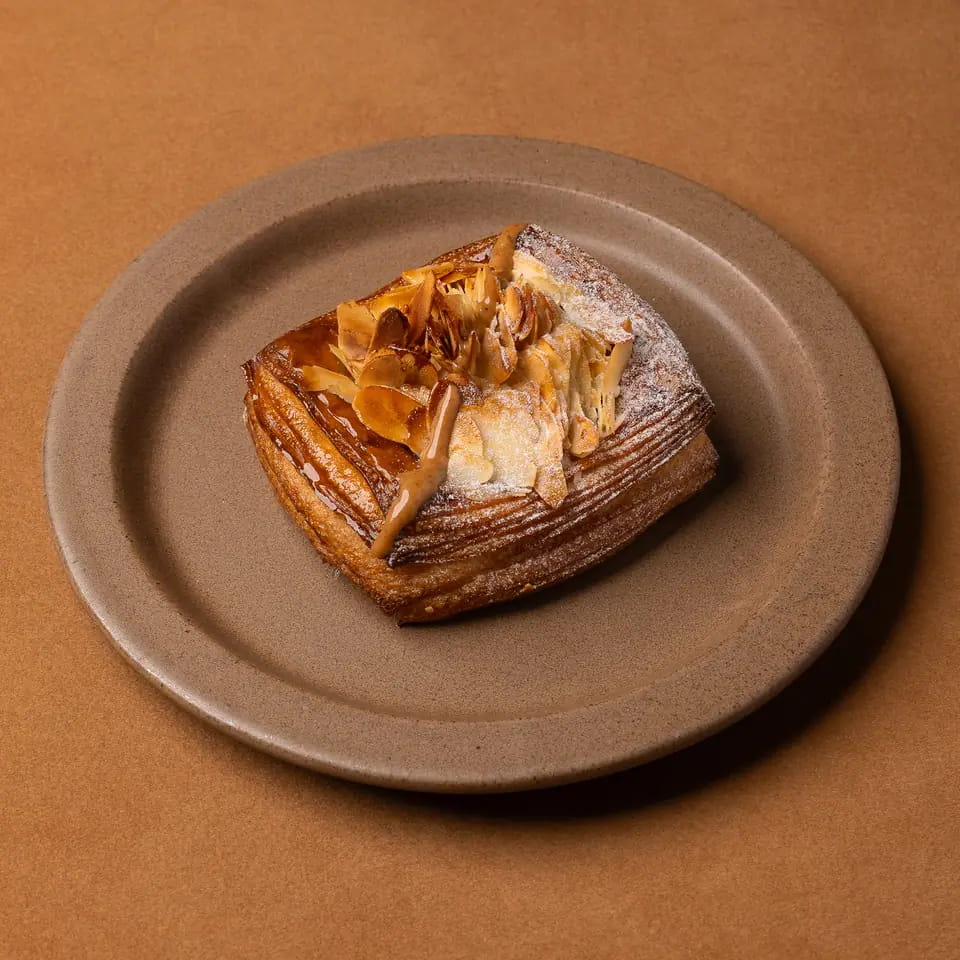 Almond danish with toasted almond flakes and icing sugar on a stoneware plate