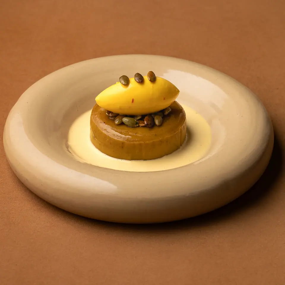 Aseeda topped with a pumpkin quenelle and seeds on a cream ring plate
