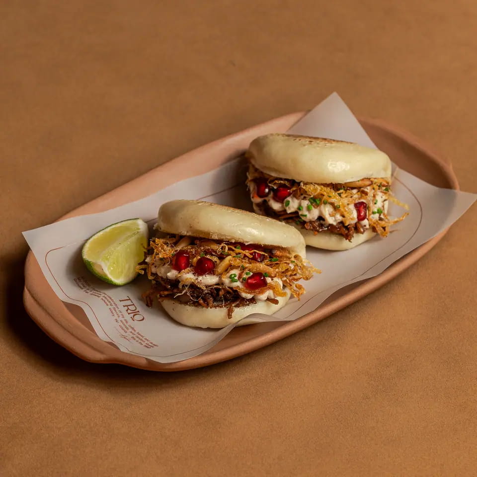Two chicken musakhan bao buns with lime on a lined tray