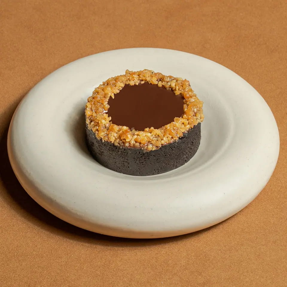 Chocolate peanut tart with a crushed-peanut rim on a cream ring plate