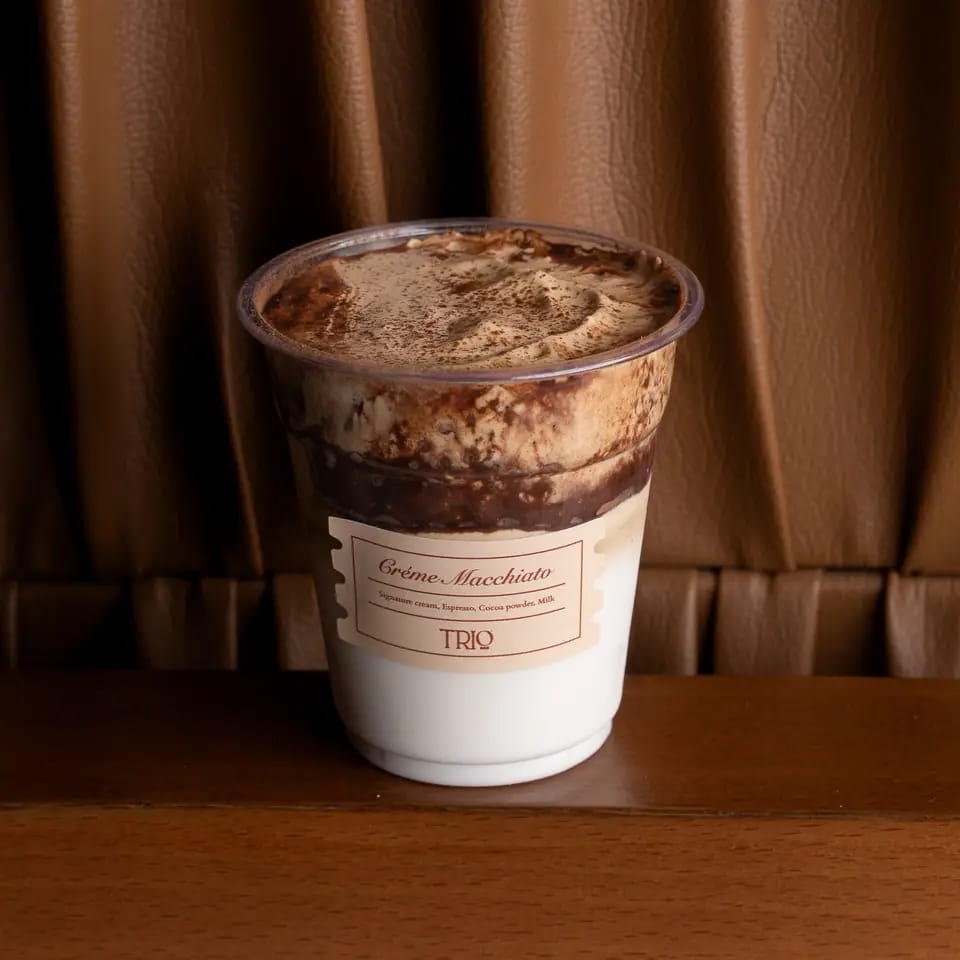Crème macchiato with cocoa-dusted foam in a takeaway cup
