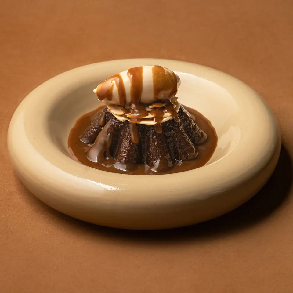 Dates pudding with caramel sauce and cream on a cream ring plate