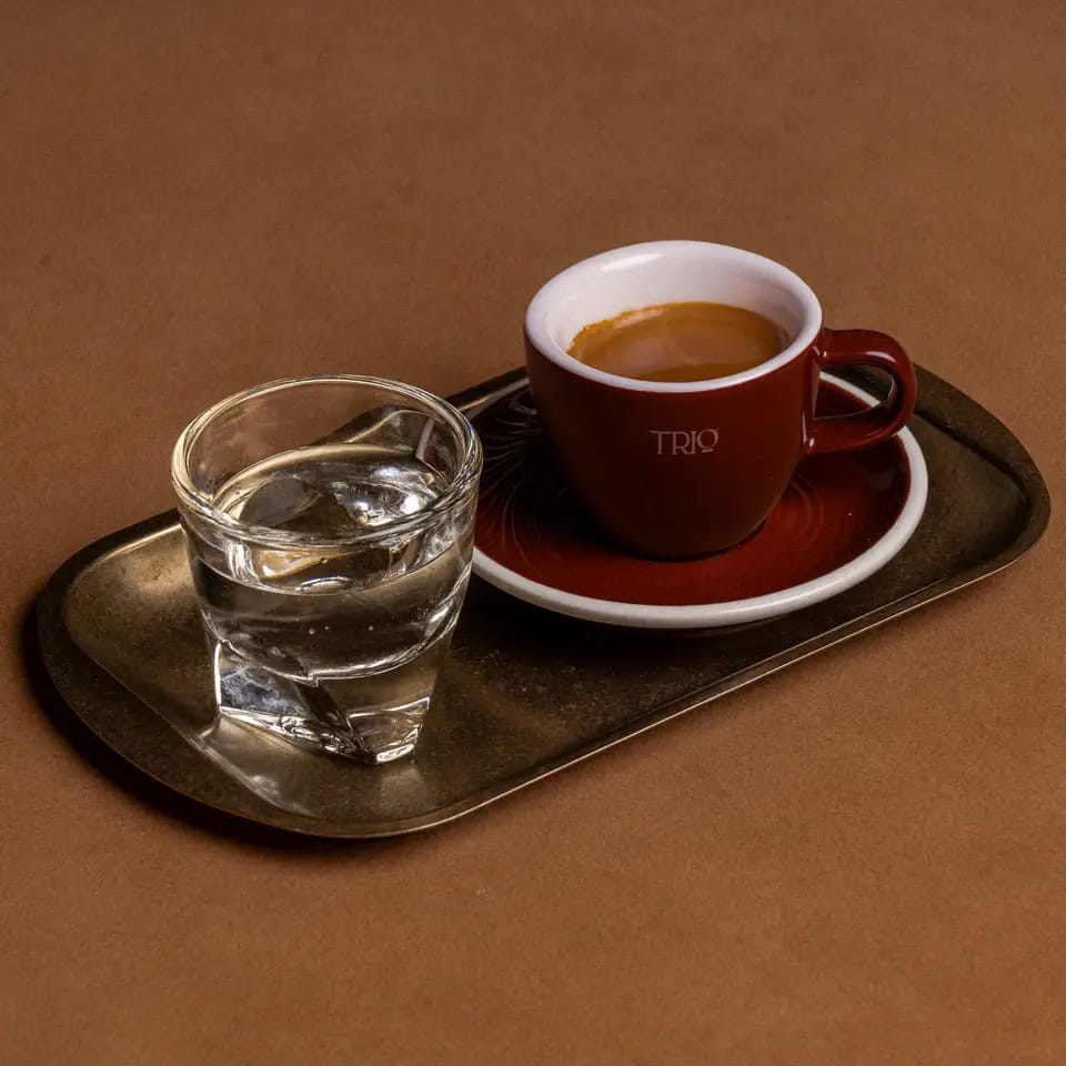 Espresso in a burgundy TRIO cup with water on a brass tray