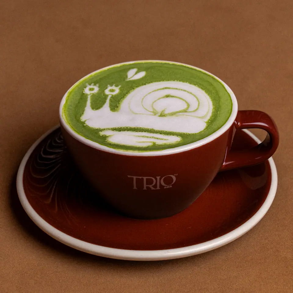 Hot matcha latte with snail latte art in a burgundy TRIO cup