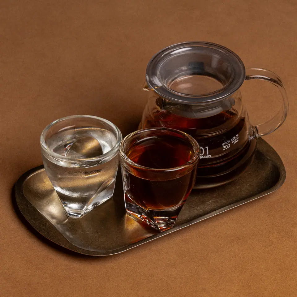 Hot V60 in a glass server with cup and water on a brass tray