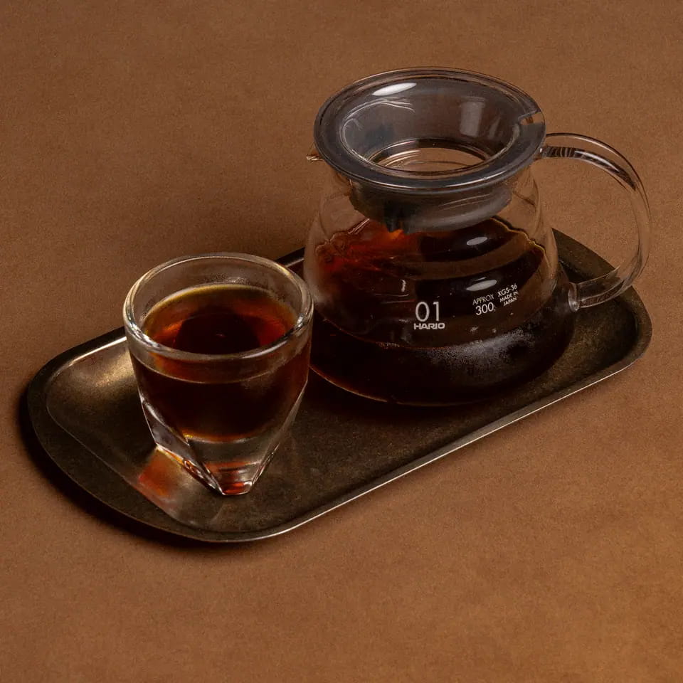 V60 in a glass server with cup and water on a brass tray