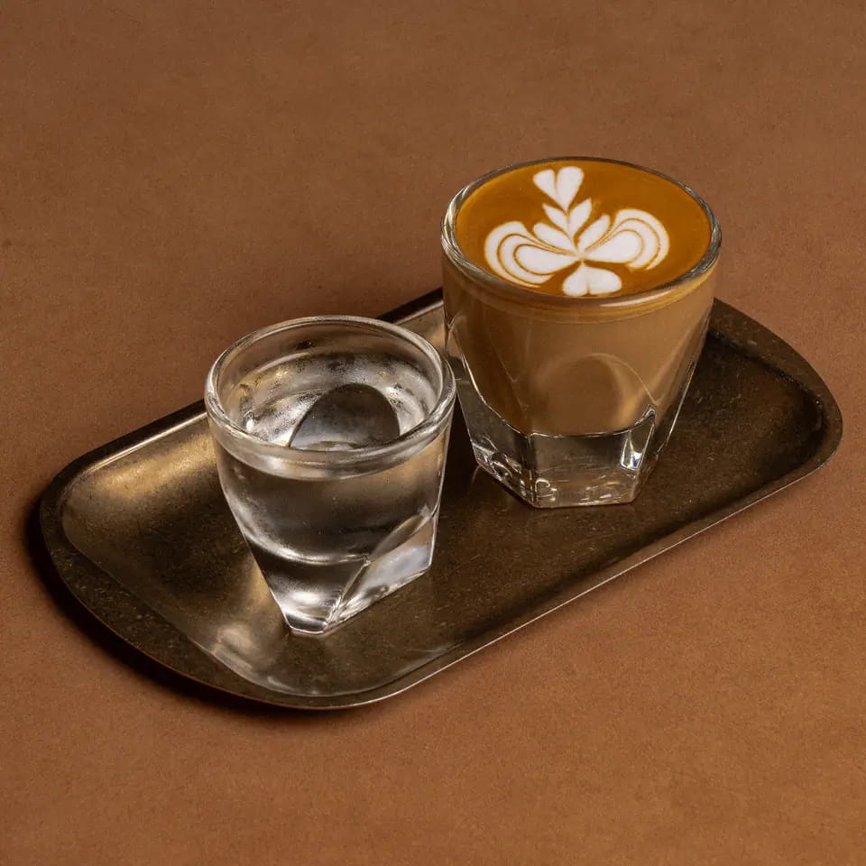 Piccolo with latte art beside water on a brass tray