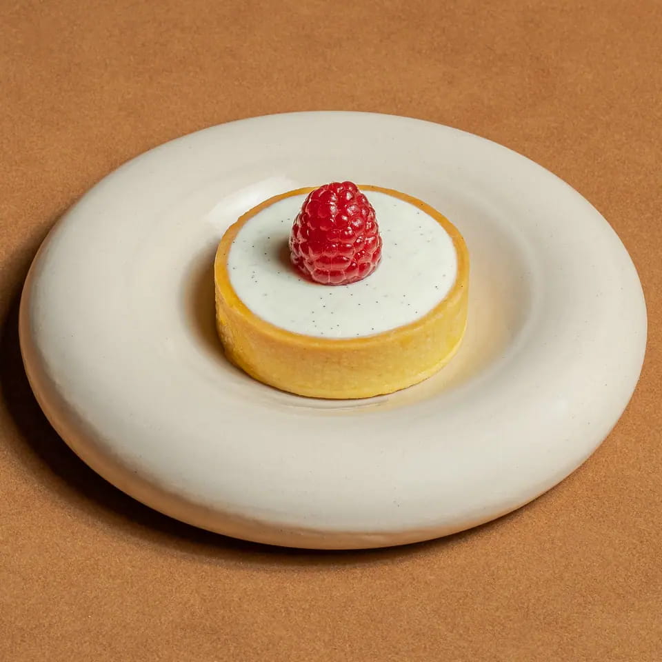 Raspberry cheesecake tart topped with a raspberry on a cream ring plate