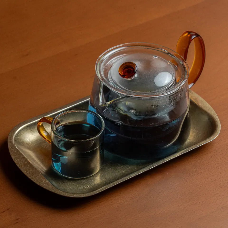 Blue sapphire jasmine tea in a glass teapot with cup on a brass tray
