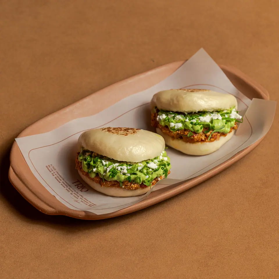 Two spicy shakshuka bao buns with herbs on a lined tray
